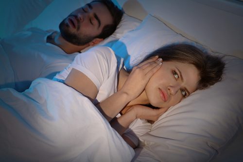 woman blocking her ears in bed while a man sleeps