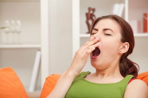 photo of a sleep deprived woman yawning in her living room