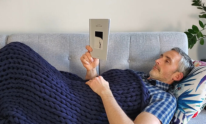 man using the Bearaby Napper while reading a book on the sofa