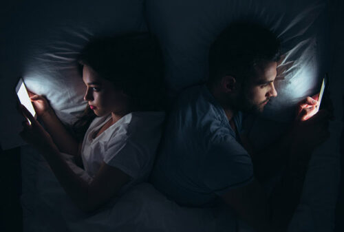 a man and woman in bed using their mobile phones