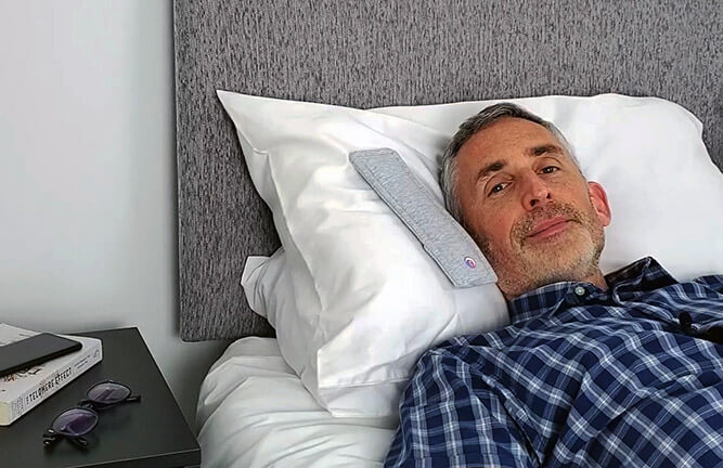 a man lying in bed with the drowsie pillow speaker on the pillow next to his head