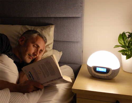 man reading in bed while using the lumie bodyclock shine 300 as a reading lamp