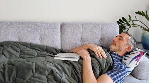 A man on the sofa asleep under a Layla weighted blanket