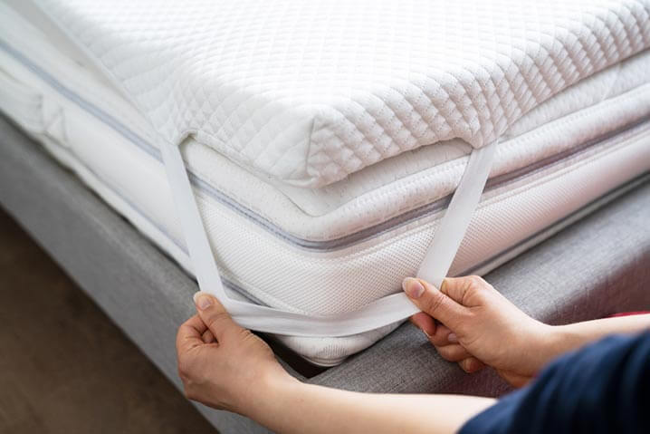 person fitting a mattress topper to a bed