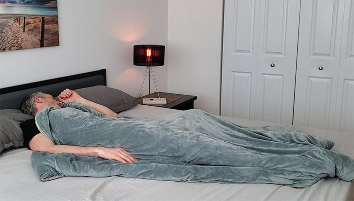 A man sleeping in bed with the Quility weighted blanket covering him