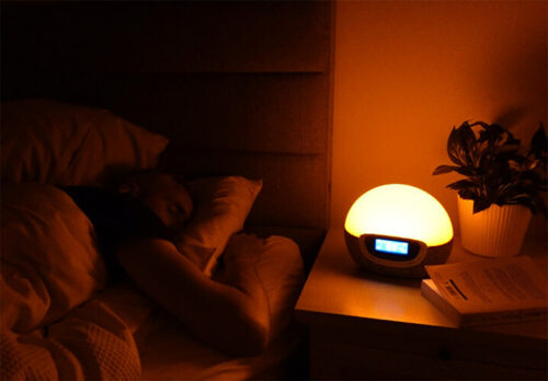 man sleeping with the lumie bodyclock shine 300 on a yellow color setting next to the bed