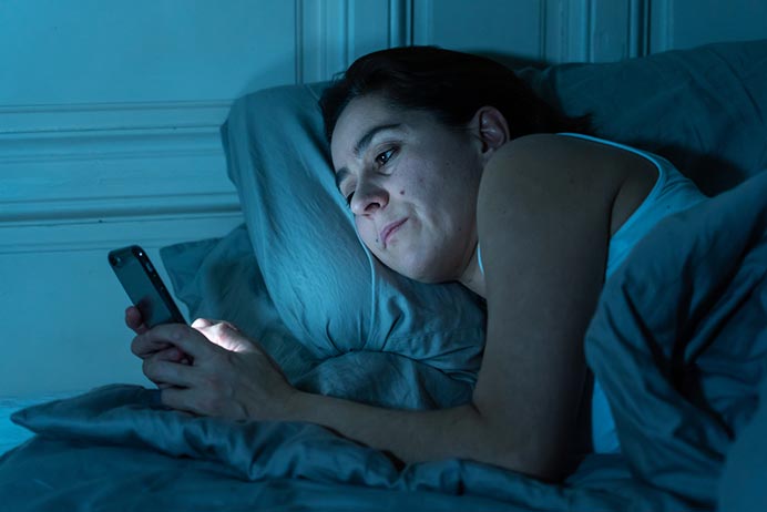 photo of a woman using her smartphone in bed at night because she can't sleep