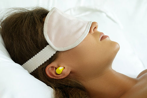 photo of a woman lying in bed wearing earplugs and a sleep mask