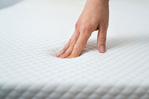 hand pressing into a memory foam mattress topper