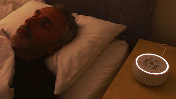 man sleeping withe Yogasleep Dreamcenter on the nightstand next to him