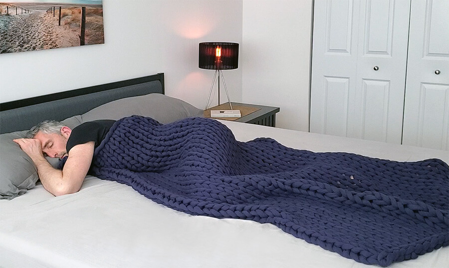 Man lying in bed with the Bearaby Cotton Napper weighted blanket on top of him