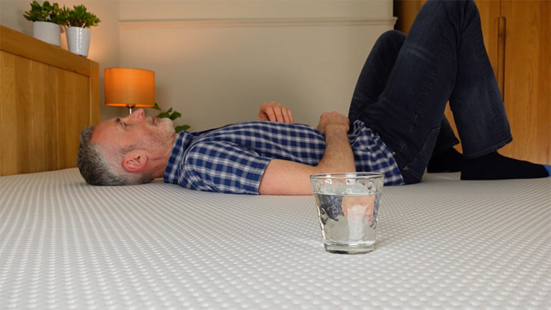 man demonstrating motion isolation of emma mattress by rolling next to a glass of water