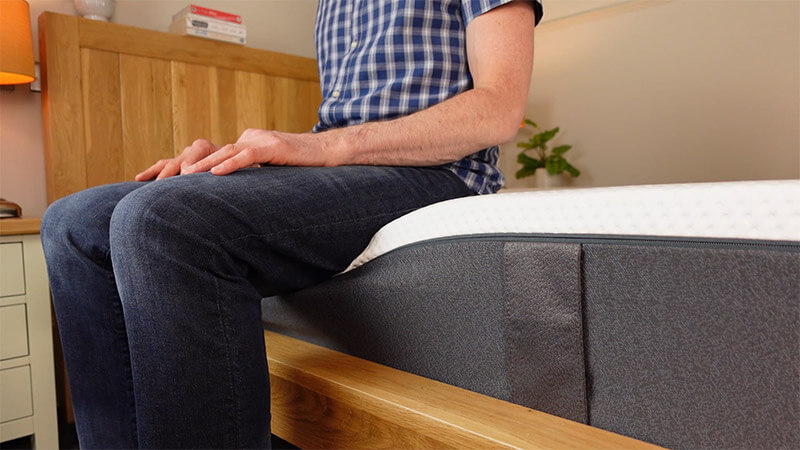 man sitting on edge of the emma mattress to demonstrate the edge support