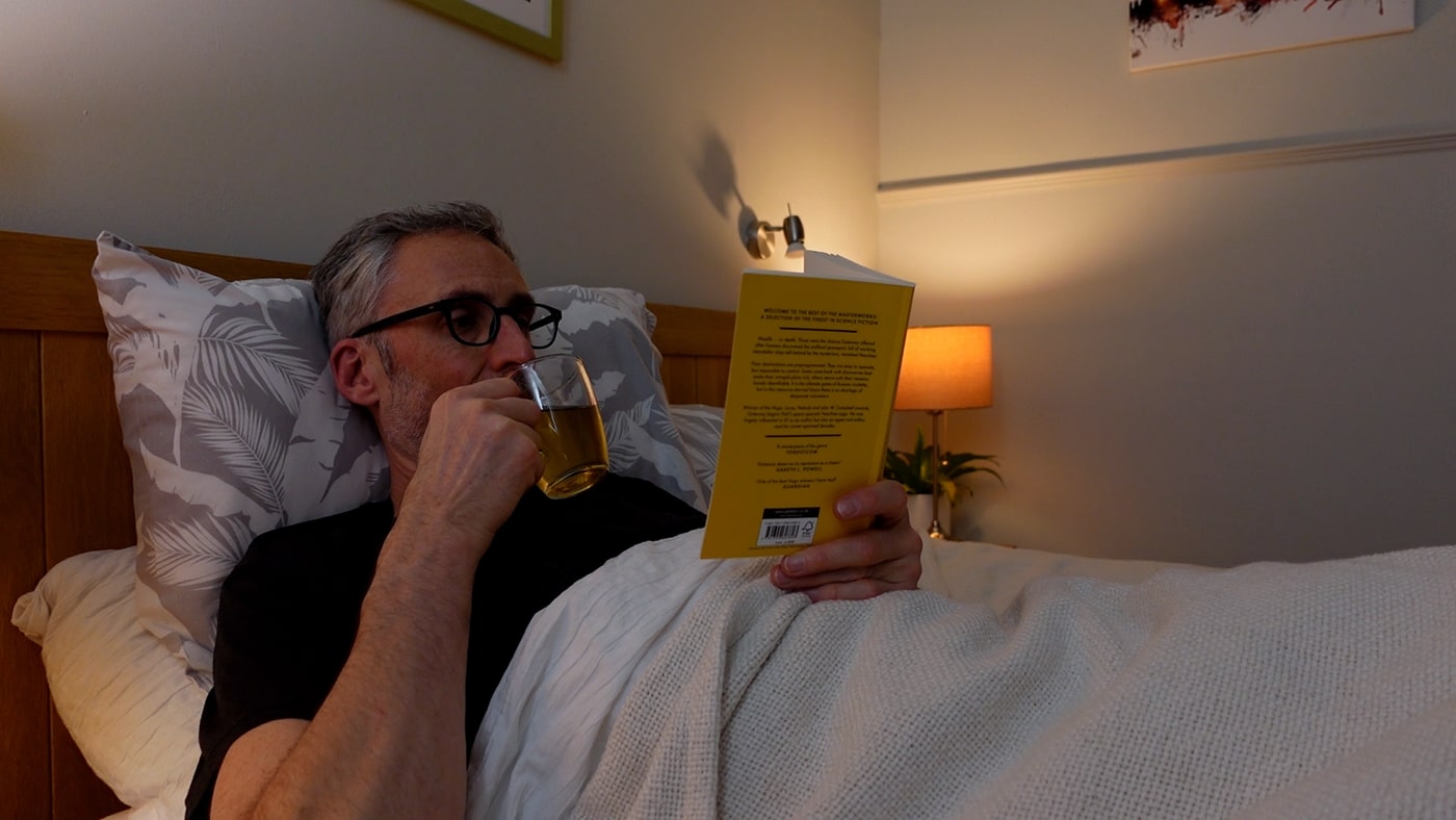 man drinking tea and reading in bed