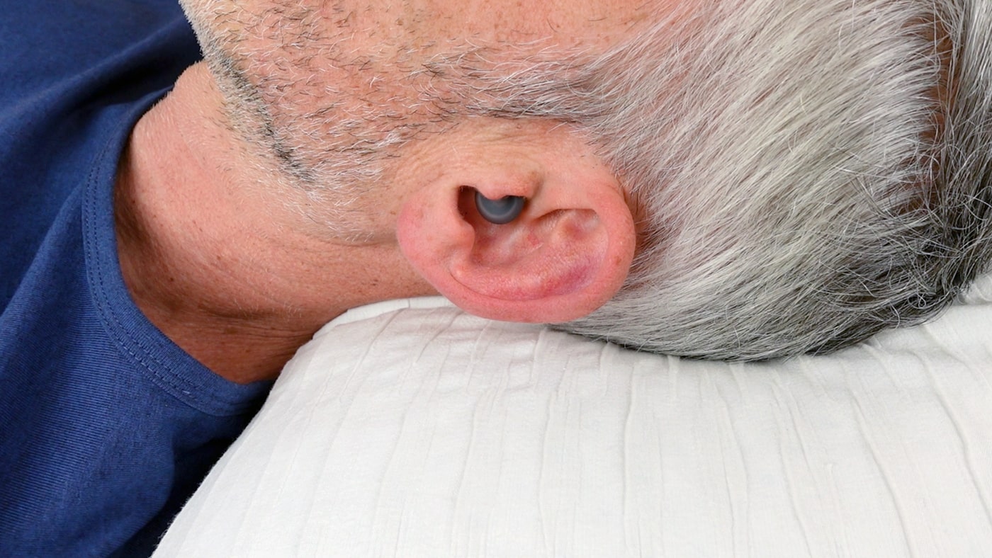left side of a man wearing Loop Dream earplugs in bed