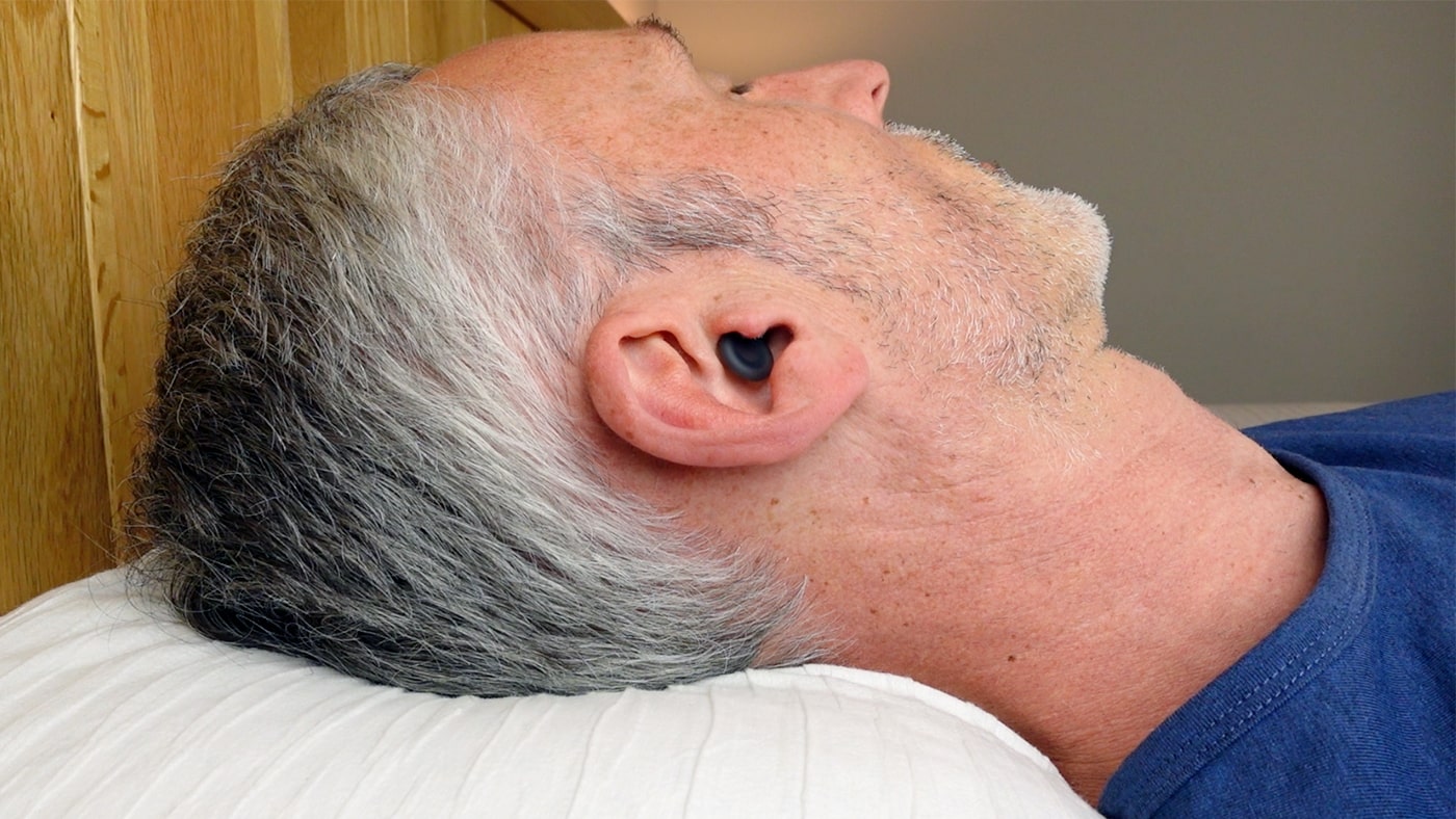 right side of a man wearing Loop Dream earplugs in bed
