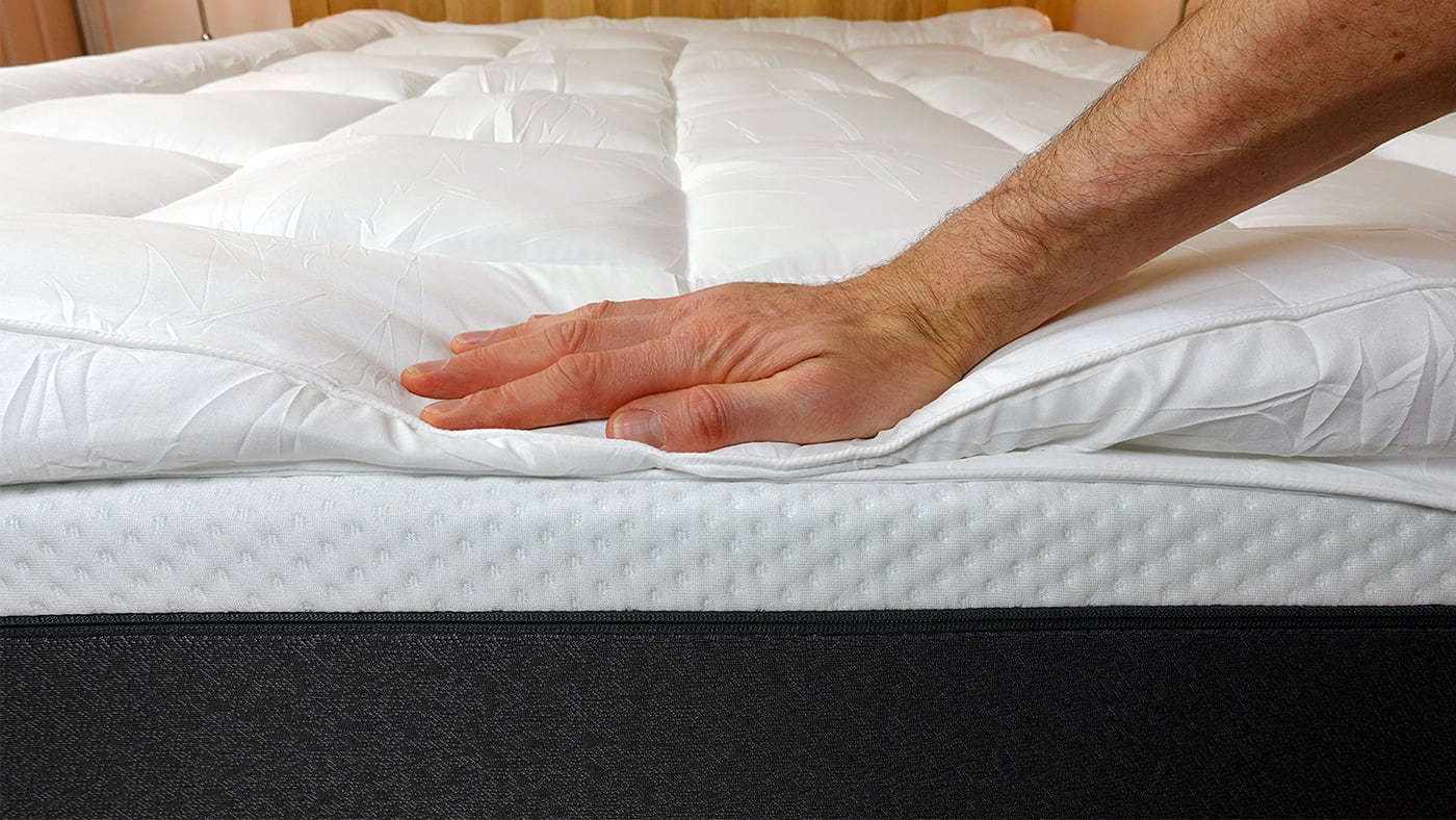 a man's hand pushing down on the MightySoft mattress topper
