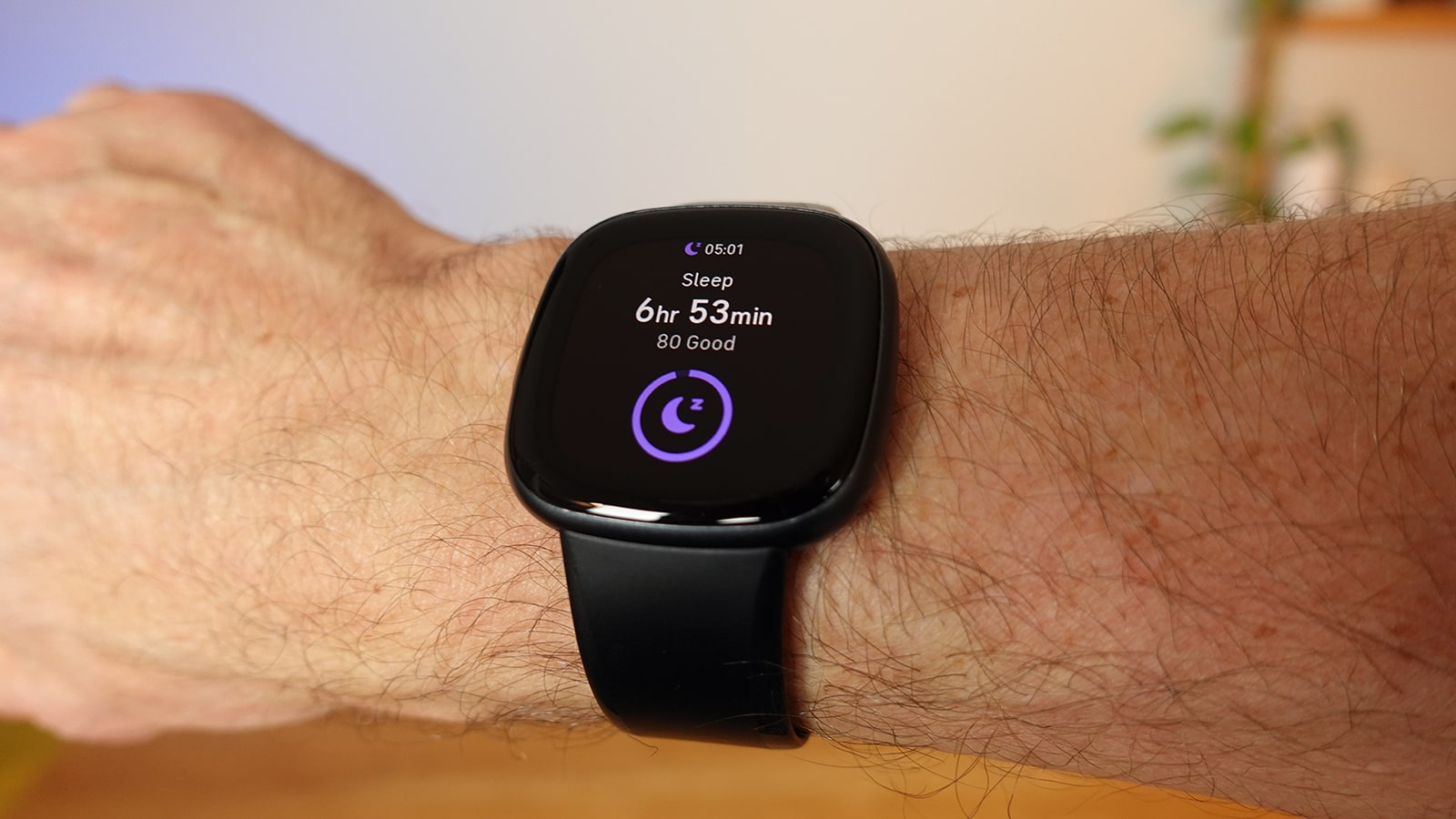 Fitbit Versa 4 on a man's wrist, with sleep data on the watch face