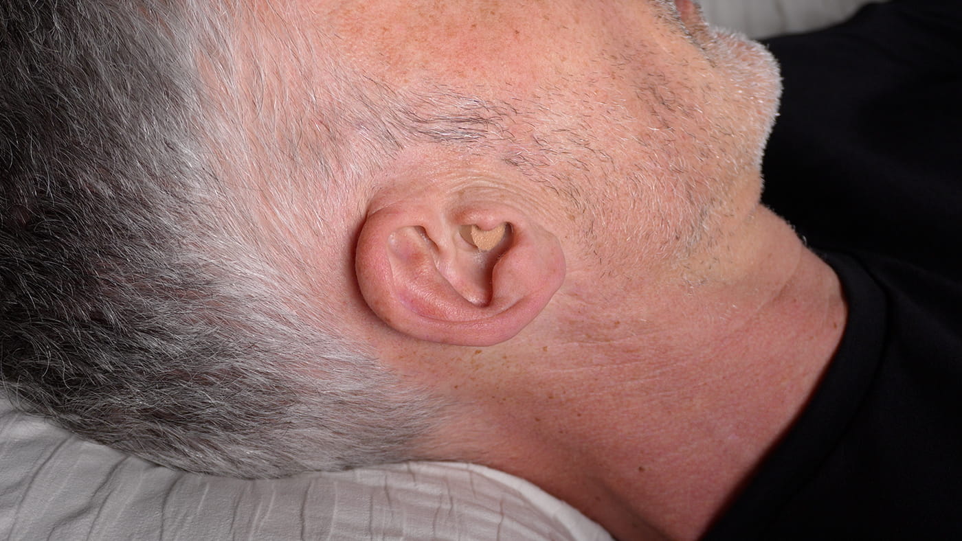 side photo of man's ear with Mack's Ultra Soft earplugs